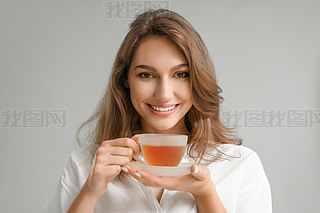 Beautiful young woman with cup of tea on grey background