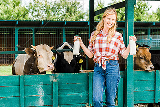 beautiful farmer showing bottles of cow milk near stable 