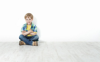 Handsome little boy sitting on floor leaning against white wall