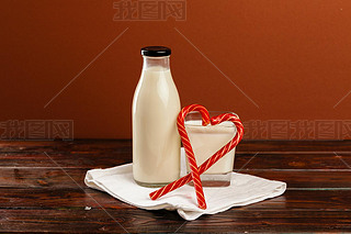 Glass bottle of fresh milk and candy canes on wooden table