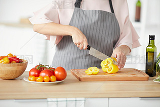 Close-up of woman in apron cutting fresh vegetables with knife on cutting board for salad
