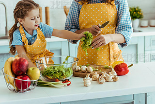 mother in polka dot yellow apron giving daughter sliced lettuce