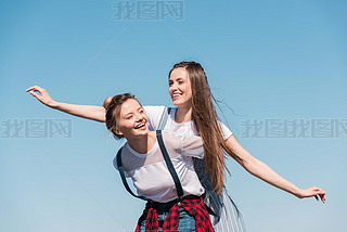 iling young woman doing piggyback ride to female friend 