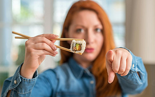 Redhead woman eating sushi using chopsticks pointing with finger to the camera and to you, hand sign
