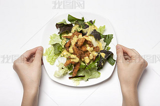 Woman hand hold a dish with salad on the white table.