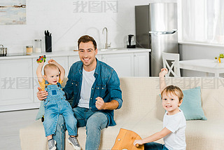 happy father looking at camera while spending time and playing with cheering preschooler and toddler