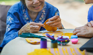 Elderly woman with caregiver in the needle crafts occupational therapy for Alzheimers or dementia