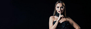 panoramic shot of scary vampire girl in black gothic dress showing shh sign isolated on black