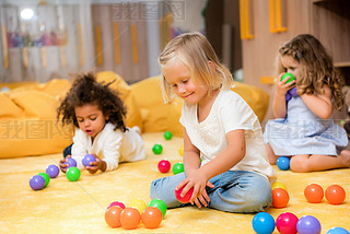 adorable multicultural kids playing with colored balls on floor in kindergarten