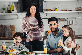 cheerful latin mother holding plate with food near cute son, husband and daughter during lunch