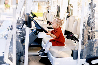 Cute 2-year old is sitting in the drivers seat of a golf cart