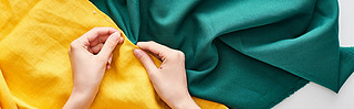 panoramic shot of seamstress sewing colorful fabric with needle 