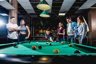 Group of young cheerful friends playing billiards. Funny time after work