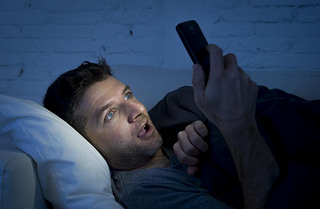 man in bed couch at home late at night using mobile phone in low light watching online porn