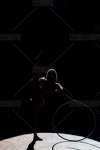 silhouette of flexible acrobat standing with hula hoop in arena of circus 