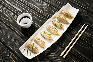 delicious Chinese boiled dumplings on plate near chopsticks and soy sauce on black wooden table