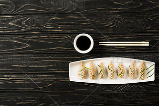 top view of delicious Chinese boiled dumplings on plate near chopsticks and soy sauce on black woode