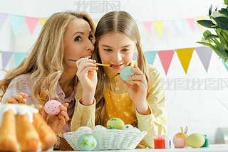 selective focus of mother iling near cheerful daughter painting easter egg 