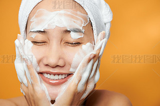 Gentle half-naked woman wrapped in towel washing her face with f