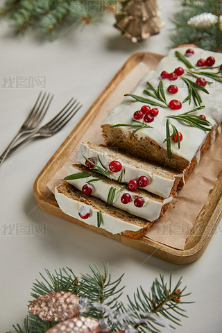 traditional Christmas cake with cranberry near forks, baubles and pine on white table