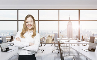 Smiling beautiful business lady with cross hands is standing in a modern panoramic office in New Yor