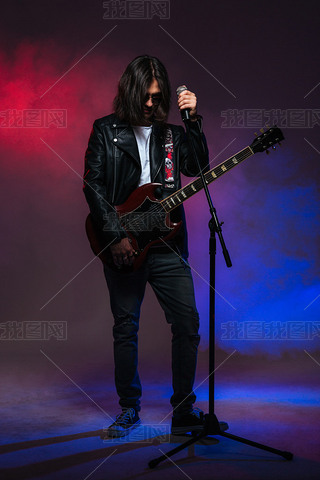 Singer with long hair singing in microphone and playing guitar 