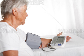 Elder woman measuring blood pressure with automatic manometer at