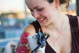 tattooer showing process of making a tattoo on young beautiful hipster woman with red curly hair han