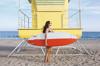 Woman standing with surfboard near the lifeguard house