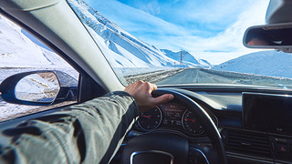 snowy mountains road view from the modern luxury car interior with drivers hand on steering wheel