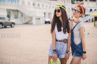 Two beautiful young girls on a skateboard in the city.