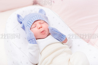 Cute little baby wearing knitted blue hat with ears and mittens lying in beautiful cradle with close