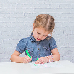 孩子, 一个女孩在桌子上写道, 画在一张纸上, 靠在一堵白色的砖墙