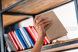 Cropped shot of student holding book at bookshelf in library 