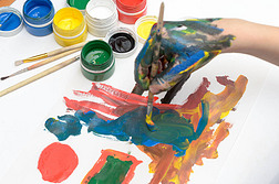 一只孩子的手在颜料上画水彩画在白纸上.