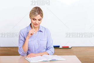 Teacher at the desk checking her register.