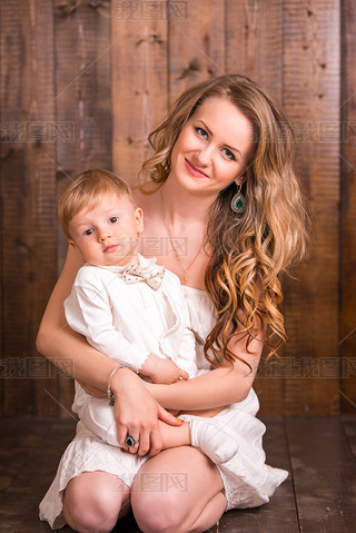 baby blond boy in a white suit white socks with his mother on a wooden background. next to a all d