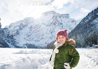 Happy child in green coat standing in front of snowy mountains