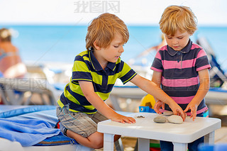 Two little kid boys playing on beach with stones