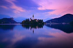 黄昏之光, 流血, 斯洛文尼亚。湖岛, 圣马丁天主教教堂和城堡山脉, 斯洛文尼亚, 欧洲。湖上的秋季风景。绿色树叶在前景.