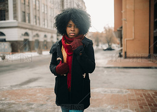 Young black woman is standing at city street against background of buildings.