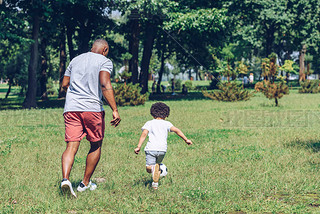 back view of african american father and son playing football in park