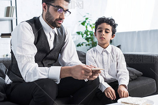 Jewish father holding matza and son looking at it in apartment 