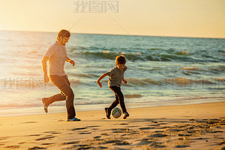 Happy father and son play soccer or football on the beach in sunset light