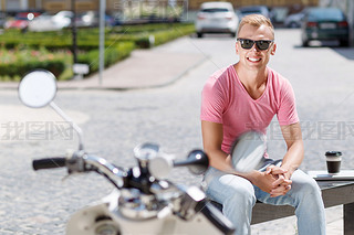 Handsome man sitting with coffee near his scooter 