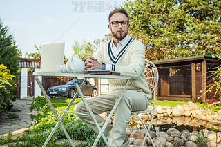 Young stylish handsome man in bright confidential clothes work at iron table with computer  teapot 