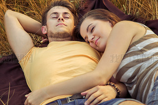 Loving couple lying down on floral field in autumnal park, warm sunny day, enjoying family, romantic