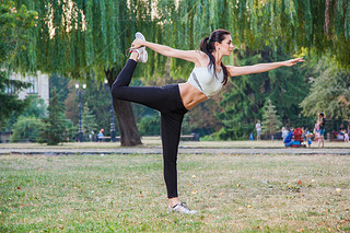 Young happy beautiful y girl is stretching in the park garden. people background. with dark hair 