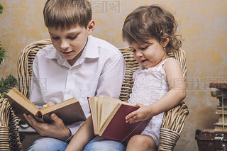 Cute babies boy and girl in a chair reading a book in a interior