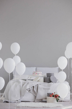 优雅的卧室配有特大号床、灰色床上用品、生日蛋糕和白色气球, 真正的照片, 空墙上有复制空间